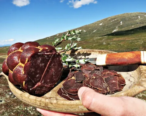 rökt kött på ett träfat och en kniv, fjäll i bakgrunden